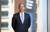 uci health president and ceo chad t. lefteris standing in front of a window wearing a blue tie white shirt and dark sport coat with uci medical center in the background