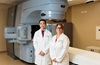 Dr. Quoc-Anh Ho and Dr. Regiane De Andrade wearing white coats and standing side by side in front of an external radiation beam machine at uci health chao family comprehensive cancer center fountain valley