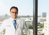 Dr. Stefan Ciurea stands in front of a window that overlooks the grounds of UCI Medical Center.