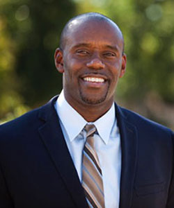 Vasco Deon Kidd, DHSc. Director of Advanced Practice Providers at UCI Health smiling standing outside wearing a dark suit