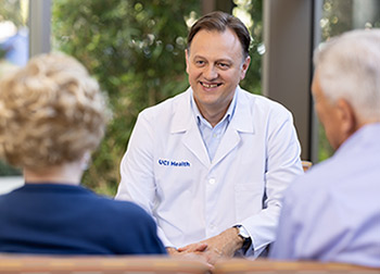 Dr. Stefan O. Ciurea, director of the UCI Health bone marrow trransplant and cellular therapy program, in white coat at center, meets with a patient and loved one.