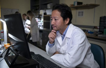 Kei Igarashi, Chancellor’s Fellow and associate professor of anatomy and neurobiology at uc irvine school of medicine, inside a lab wearing a white coat and looking at a computer