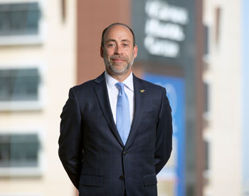uci health president and ceo chad t lefteris, one of america's CEOs to know, wearing a dark suit light blue tie standing in front of a window with uci douglas hospital in the background