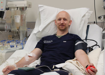 a platelet donor at uci health - irvine wearing dark blue scrubs holding a red ball with tubes and a blood pressure cuff on his arms