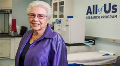 claudia kawas in the all of us lab wearing a purple top in front of a sign that says all of us research program