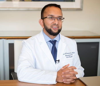 uci health gastroenterologist dr jason b samarasena sits at a desk wearing a blue tie and shirt and a white coat