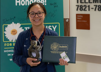 uci health nurse rosey vu holder her daisy award certificate and healer's statue in front of the daisy sign