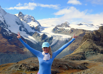 suzette kirby in front of snow-capped mountains wearing a blue shirt with her arms outstretched