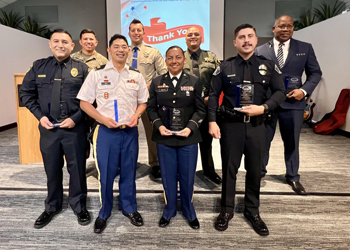 uci health los alamitos director of plant operations santiago chambers holding his front line hero award with other winners; santiago is in the back right wearing a dark suit and tie