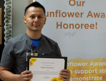 uci health nurse rafeal mendoza holding his sunflower award certificate in front of a sign saying congratulations to our sunflower award honoree
