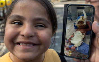 Eight-year-old Sarah Parra is all smiles as her mom, Dora Leon, holds a cellphone picture of her daughter when she was born at 24 weeks and weighed one pound. Sarah spent 6 months in the neonatal intensive care unit at UCI Medical Center. They were at the Reunion Carnaval in Orange on Sunday, Oct. 6, 2024. (Photo by Mindy Schauer, Orange County Register/SCNG)