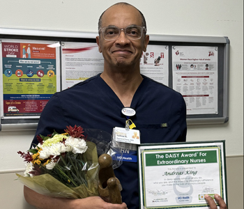 uci health fountain valley nurse andreas king wearing scrubs holding his daisy certificate, flower bouquet and healer's touch statue