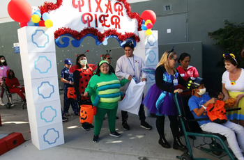 kids dressed up as their favorite characters walk in a pediatric halloween parade at uci health fountain valley under a colorful sign saying pixar pier photo credit James Carbone of the daily pilot