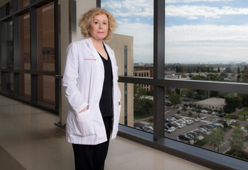 uci health hematologist oncologist dr. susan obrien wearing a white coat stands in the hallway of uci douglas hospital in front of a window overlooking uci medical center in orange, part of uci health