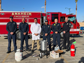 uci health burn director dr syed saquib stands with anaheim fire department firefighters in front of a red fire truck standing behind a turkey fryer and propane tank