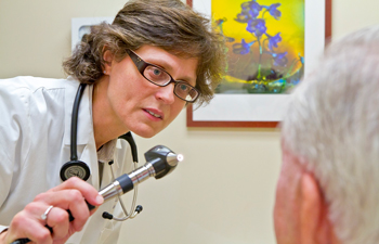 uci health geriatrician dr lisa gibbs wearing a white coat and stethoscope holds an eye exam scope while looking at a patient