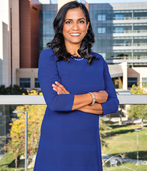 uci health gastroenterologist dr Nimisha Parekh wearing a blue dress is standing with her arms crossed in front of uci medical center Carla Rhea for Orange Coast