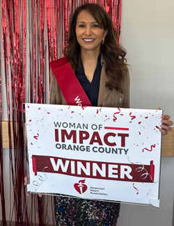 uci health susan samueli integrative health institute director shaista malik is the american heart association's woman of impact winner; she holds a sign and wears a sash honoring her