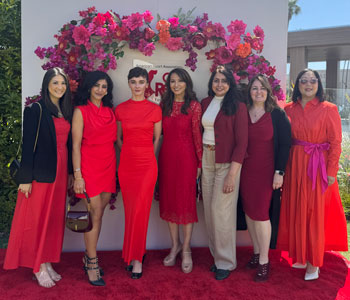Leaders from UCI Health and UC Irvine dressed in red in front of a flower arch at the american heart association go red for women luncheon in may 2025