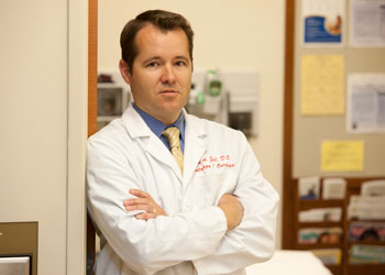 uci health hematology oncology and colorectal cancer specialist dr jason zell wearing a white coat in an office and leaning against a door