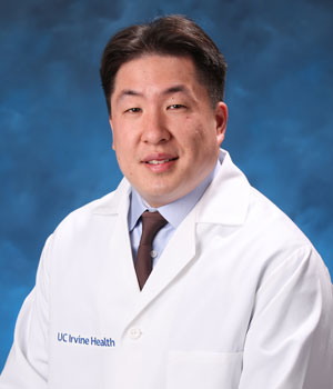 uci health neurologist and multiple sclerosis specialist dr michael sy wearing a white coat in front of a blue studio background