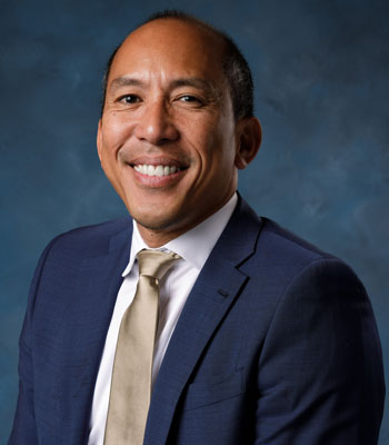 uci health chief financial officer and senior vice president randolph siwabessy in a dark suit in front of a blue studio background