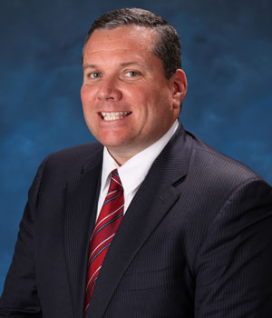 uci health psychiatrist dr robert mccarron wearing a suit and sitting in front of a blue studio background
