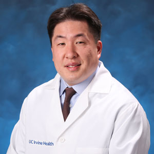 uci health neurologist dr michael sy wearing a white coat in front of a blue studio background
