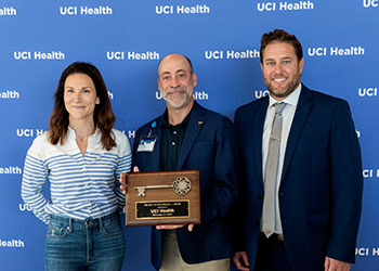 Chad T. Lefteris, president and CEO of UCI Health, (center) poses with a commemortive key to UCI Health — Irvine, a new acute care hospital sent to open Dec. 10, 2025, as Hensel Phelps construction supervisor Kasie Bowden, left, and the company's operations manager, Brian Maximuk, look on. .