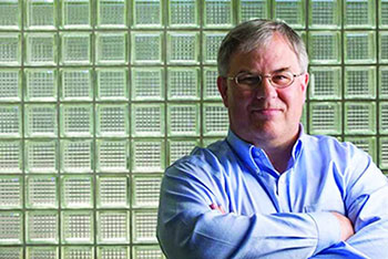Dr. Michael Demetrious, UCI Health neurologist and cancer researcher, stands with arms folded against a glass block wall.