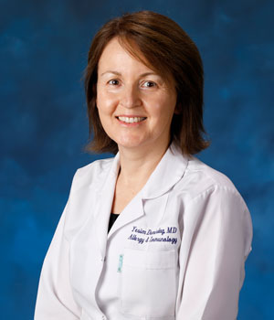 uci health allergist and immunologist dr yesim demirdag wearing a white coat in front of a blue studio background 