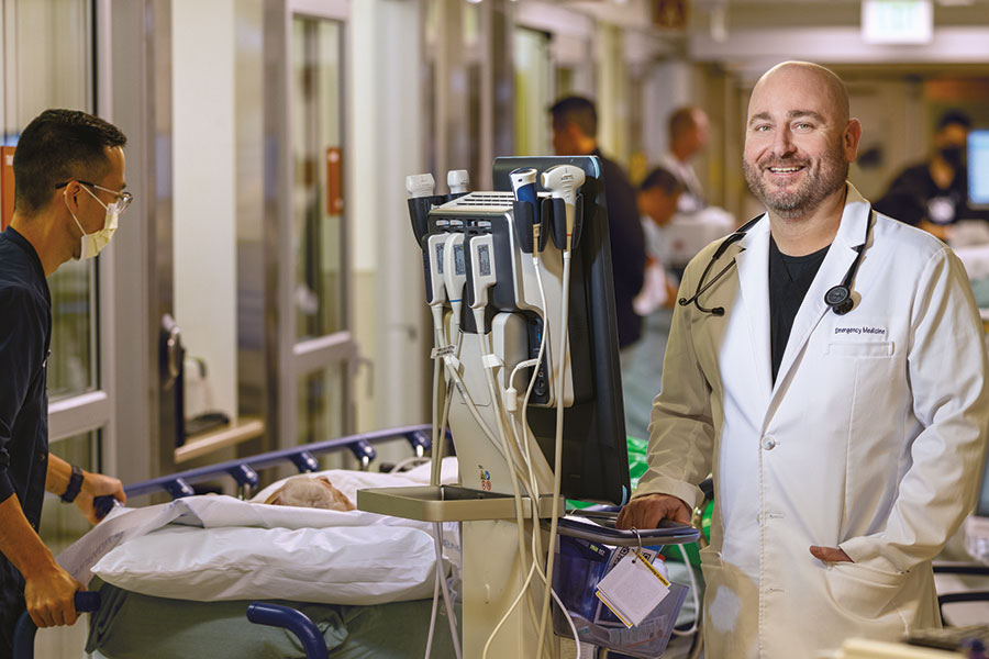 UCI Health Emergency medicine specialist Dr. Ryan Gibney wearing a white coat stands in a busy emergency room hallway.