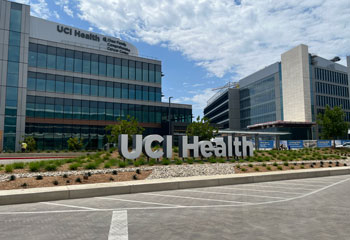 exterior of the uci health chao family comprehensive cancer center and ambulatory care building with a uci health sign next to the uci health irvine acute care hospital on a sunny day with clouds
