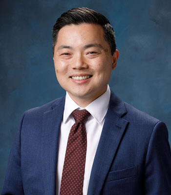uci health chief operating officer and senior vice president nathan shinagawa in a dark suit in front of a blue studio background