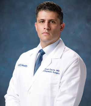 studio shot of uci health orthopedic surgeon dr. jonah davies wearing a white coat in front of a blue studio background