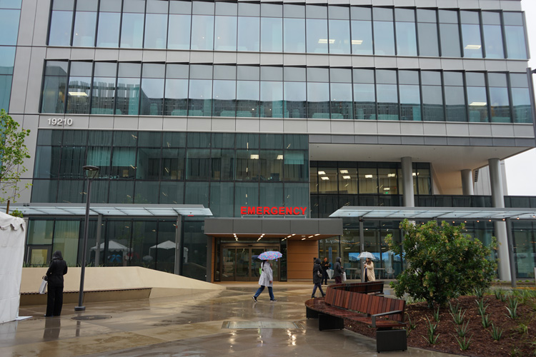 a person walks by holding an umbrella outside the uci health irvine acute care hospital 24 hour emergency room