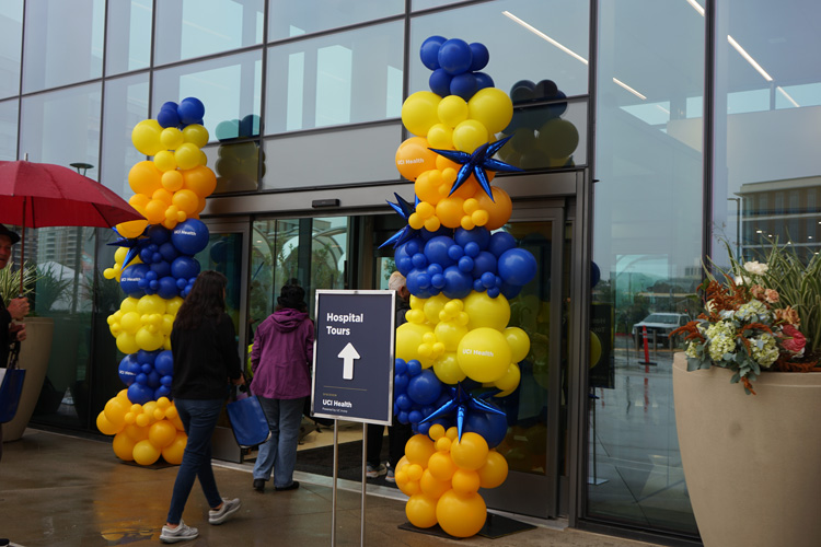people walk into exterior of uci health irvine acute care hospital on cloudy rainy day next to balloon arrangements