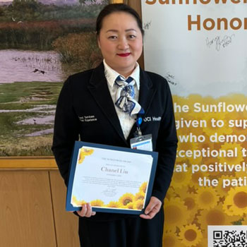 uci health sunflower award winner chanel liu holds her award certificate and stands in front of the sunflower winner sign