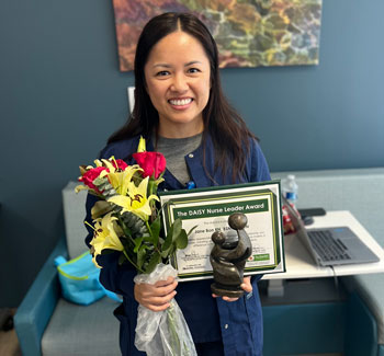 uci health daisy winner jane bon celebrates her honor while holding her healer's touch sculpture and a certificate