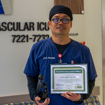uci health orange daisy award winner rhodel aratep holds is award certificate and sculpture while wearing scrubs