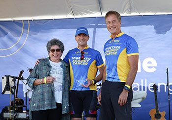 Bransby Whitton, center, is honored at the 2025 UC Irvine Anti-Cancer Challenge event. He is flanked on the left by his oncologist Dr. Lauren Pinter-Brown and Anti-Cancer Challenge founder Dr. Richard Van Etten on the right.
