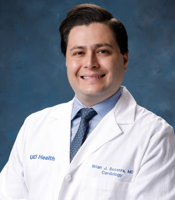 uci health cardiologist dr brian becerra in a white coat in front of a blue studio background