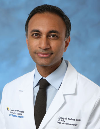 uci health ophthalmologist dr sanjay kedhar wearing a white coat in front of a blue studio background
