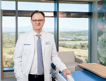 Dr. Stefan O. Ciurea, wearing a white coat, stands in a patient room at the new Irvine hospital with a view of the San Joaquin Marsh Reserve behind him.