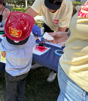 a young burn survivor wearing a fireman's hat attends the burn scar print workshop at the annual uci health burn picnic on june 28