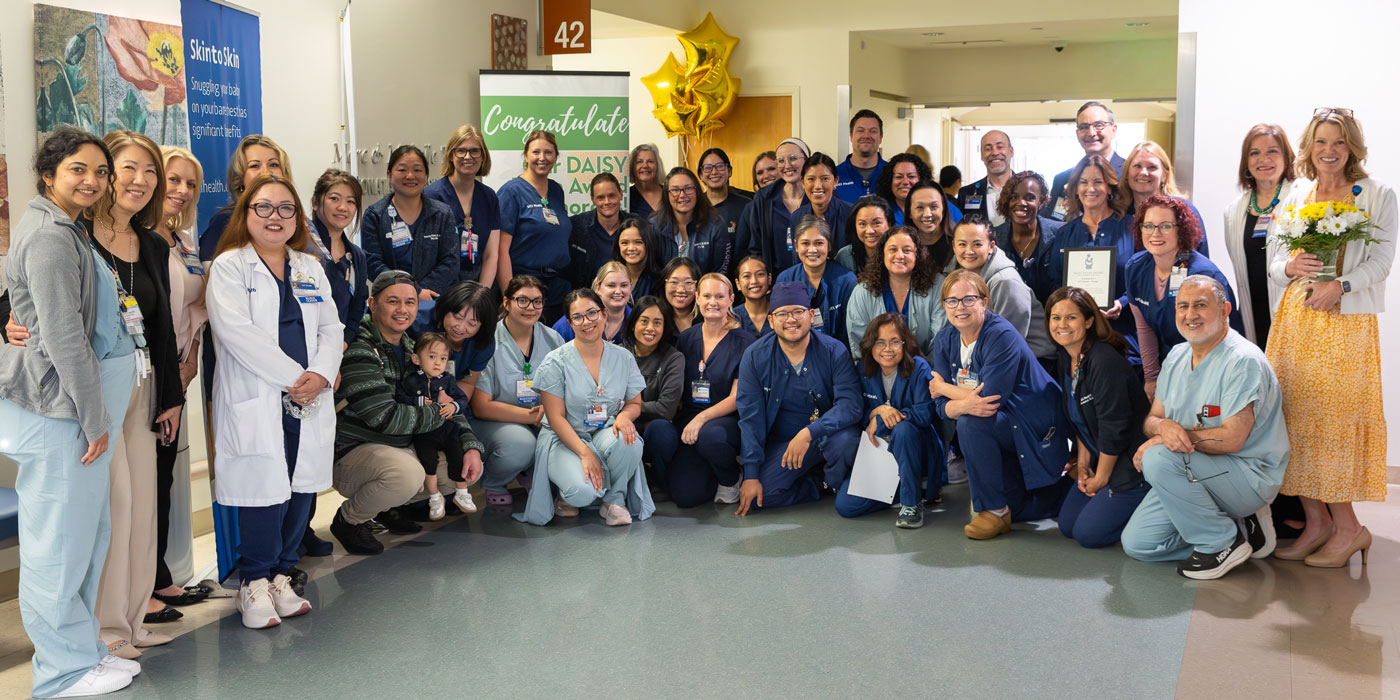 the uci health neonatal intensive care unit (nicu) team and leadership gather for a group photo in a hospital hallway to celebrate their daisy team award