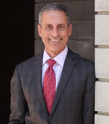 dr michael stamos, dean of the uc irvine school of medicine and interim vice chancellor of health affairs, leans against a wall outdoors while wearing a suit
