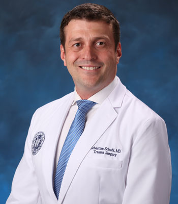 uci health trauma and critical care surgeon dr. sebastian schubl wearing a white coat in front of a blue studio background