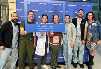 a group of uci health co-workers stand in front of a step and repeat and behind a photo frame to celebrate the opening of uci health -- irvine; dr jeffry nahmias is second from the left