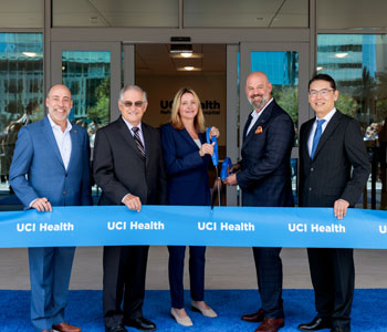uci health and lifepoint leaders stand on a blue carpet behind a blue ribbon saying uci health at the ribbon cutting for the uci health irvine rehabilitation hospital